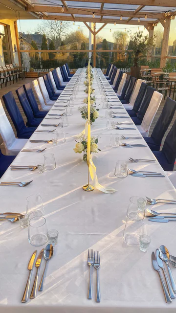 A long table laid for a celebration under the covered terrace, with navy chair covers