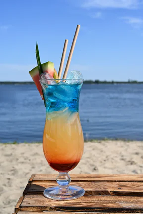 A colourful cocktail with fruit on a wooden crate on the beach, the lake behind