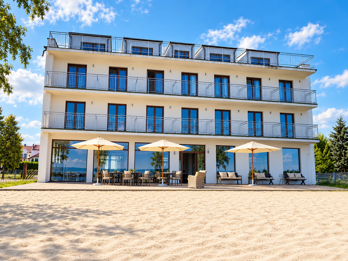The white Relax Place hotel building with balconies, a terrace with parasols and the sandy beach in front