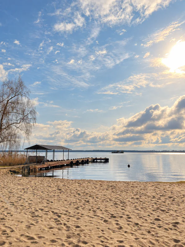 The sandy beach and a pier with a roofed shelter on Lake Zegrzyńskie on a sunny day