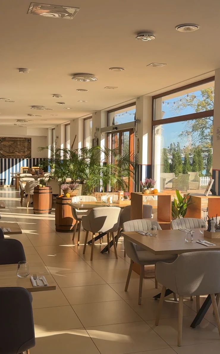 The bright restaurant dining room with wooden tables and large windows in the afternoon sun