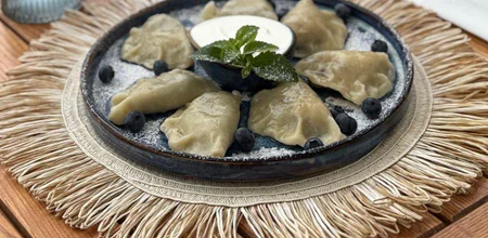 Pierogi posypane cukrem pudrem, z borówkami i śmietaną