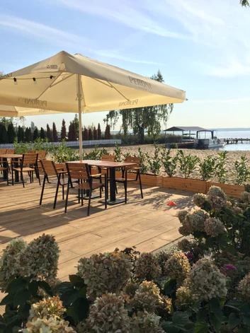 The restaurant terrace with tables under a parasol, the beach and lake beyond