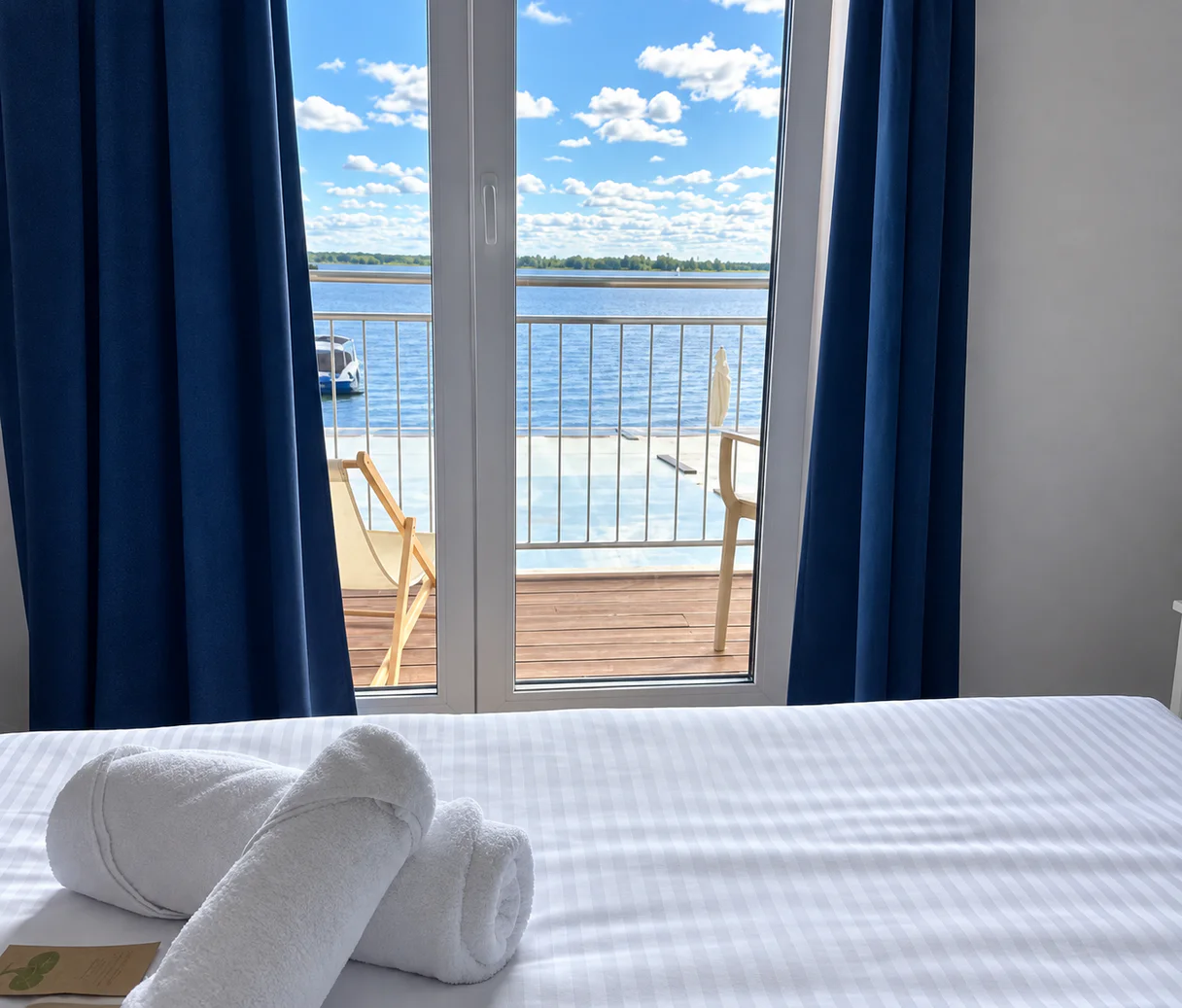 View from the bed through the balcony doors to the lake, with rolled towels on the bed