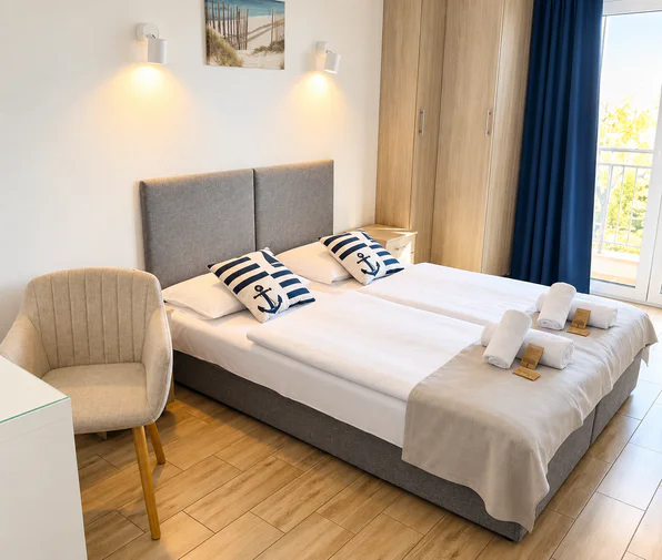Room with a double bed, anchor cushions, an armchair and a door to the balcony